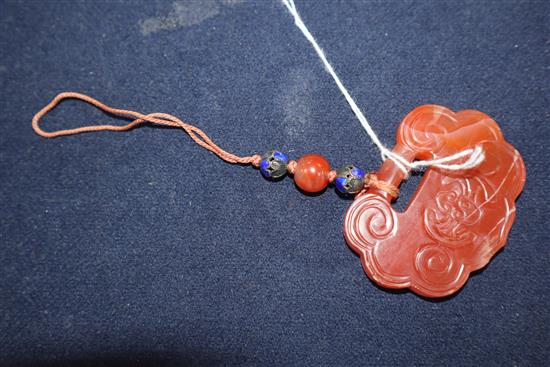 A Chien Lung red bowenite, carved and shaped disc pendant, decorated with stylised scrolls